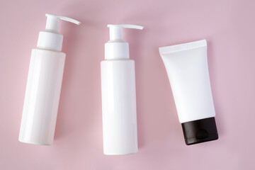 White bottles and tube of cosmetic products on pink background