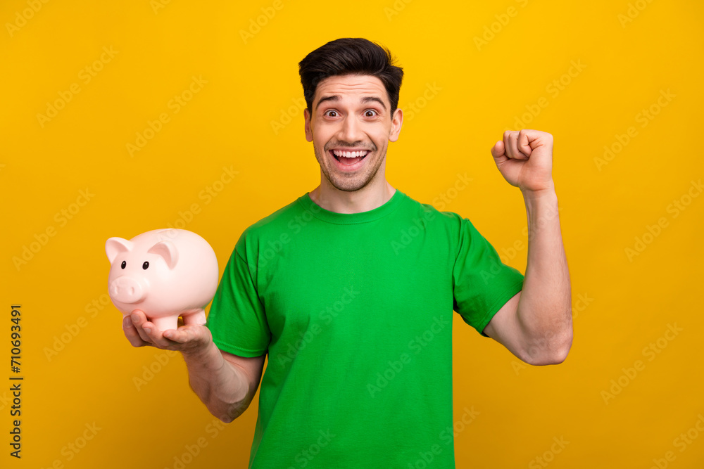 Sticker Photo of funny young guy learning financial literacy raised fist up celebrating piggy bank savings isolated on yellow color background