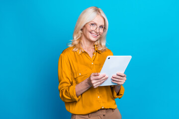 Photo portrait of lovely retired lady hold tablet remote work wear trendy orange smart casual garment isolated on blue color background