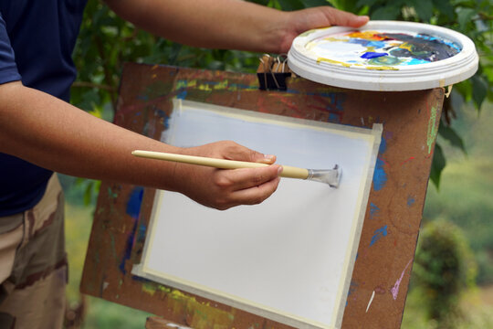 An art teacher teaches landscape painting with watercolors to children attending art camp. Soft and selective focus.