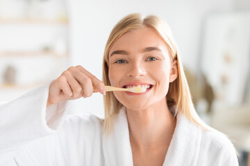Young blonde woman brushing teeth focusing on oral hygiene indoor