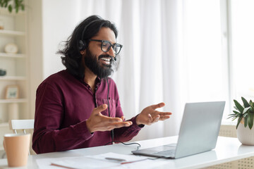 Online Tutoring. Young indian tutor wearing headset making video call on laptop