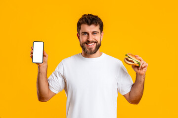 Happy guy holds burger and shows phone empty screen, studio
