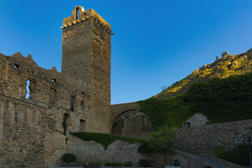 Ruins of the Monastery of Sant Pere de Rodes in Alt Empordà, with its imposing tower and walls partially covered with ivy, in contrast to the sky at sunset.