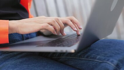 Close up of woman's hands typing on modern laptop situated on laps while sitting in public park. Concentrated female answering emails on portable device connected to free wireless internet connection.