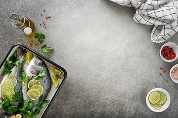 Raw fresh. Fresh raw dorado with lemon, lime, parsley and salt on old grey concrete background ready for cooking. Sea bream, dorado. Seafood, healthy food. Top view. Long banner format. - obrazy, fototapety, plakaty