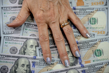 A woman's hand resting on a background of 100 US dollar notes