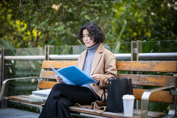 Fototapeta premium Woman sitting on park bench reading documents