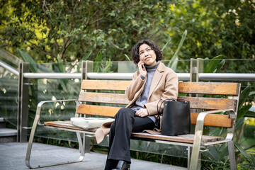 Fototapeta premium Woman talking on phone on park bench
