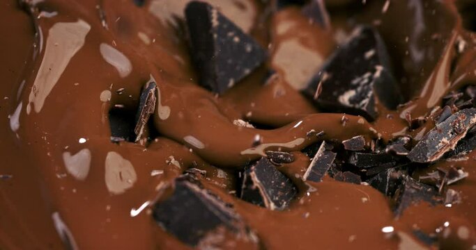 Super slow motion macro of raw bio organic dark bitter chocolate bar chunks falling in creamy melted liquid dark cocoa chocolate with splashing dripping drops at 1000 fps.