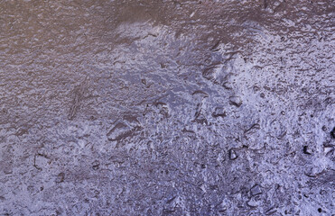 Close up of muddy puddle with small stones on wet surface. Background texture