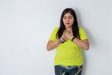 Mexican woman with sports clothing has her hands on her chest in a meditating position, with white...