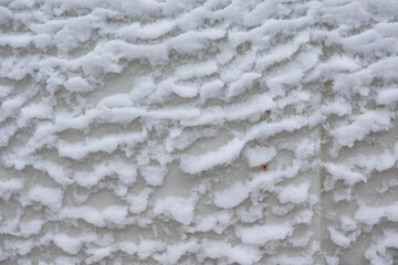 Snow flakes stuck in the form of waves on a white metal sheet. There are rust spots. Close-up. Background.