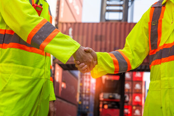 male worker wearing a reflective uniform loads a container, shaking hands with a colleague engineer...