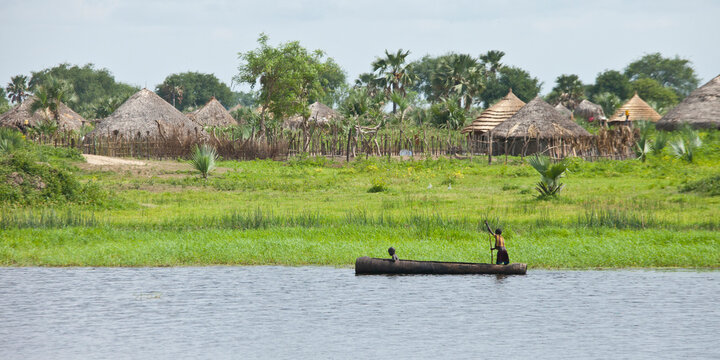 A dugout canoe goes past a village along the Nile River in South Sudan.