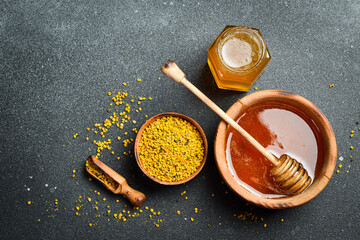 Organic honey in wooden bowl with honey stick and flower pollen. Honey background. Top view. - obrazy, fototapety, plakaty