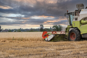 A combine harvester harvests in a wheat field against the backdrop of an epic sunset before the...