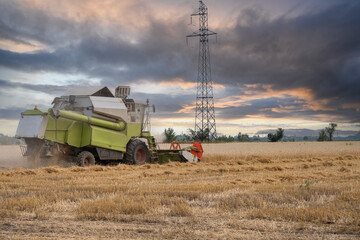 A combine harvester harvests in a wheat field against the backdrop of an epic sunset before the...