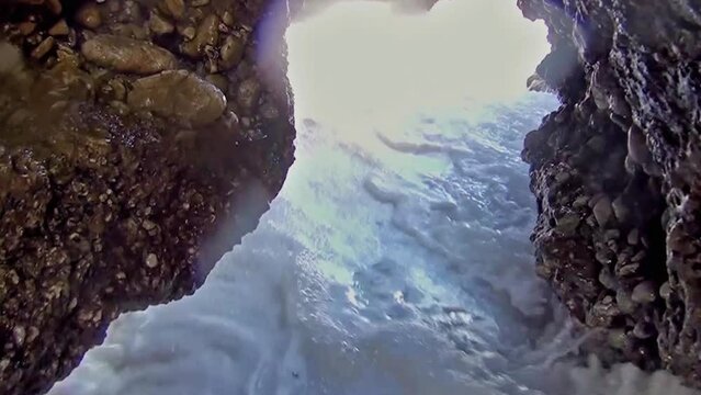 Camera quickly retreating between rocks in cliff tunnel due to the force of sea waves.