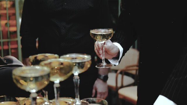 Close-up waiter hand in black gloves raises a glass of champagne from the tower for a restaurant guest, wedding, close-up hand of waiter with champagne, man in black suit, slow motion shot.