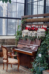A Christmas composition of an old piano with an old gold-colored chair stands in a room with large windows.