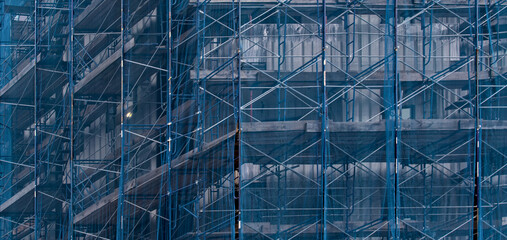 building under construction covered in blue mesh tarp protective wrap (safety debris netting during...
