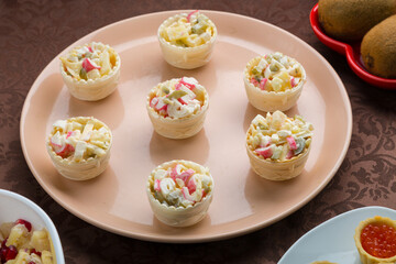 on the table is a salad in tartlets in a plate on a brown tablecloth