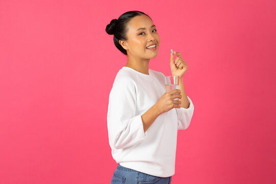 Beauty Supplements. Beautiful Young Asian Woman Holding Glass Of Water And Pill