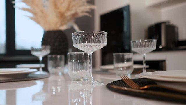 Beautiful apartment interior and kitchen design with a large dining table in boho style. On the table there are glasses, plates, spoons, forks, fruits. Romantic dinner before a couple's date