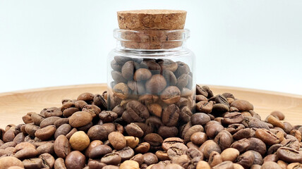 Coffee beans in a small glass jar with a cork lid on the table. Coffee beans packed in a transparent, airtight storage container. Coffee seeds inside a glass jar.