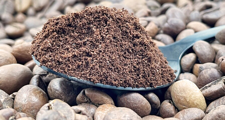 Against the background of roasted aromatic coffee beans lies a metal spoon filled with ground...