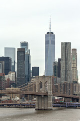 nyc skyline with brooklyn bridge and one world trade center (gray sky, cloudy overcast day)...