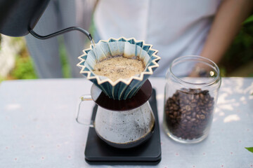 Happy Asian beautiful woman making a specialty coffee in morning at her backyard garden, woman brewing a coffee by dripping or pouring over a hot water.