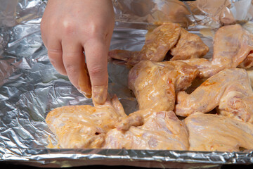 a woman's hand places chicken wings in soy sauce and garlic marinade on foil for baking