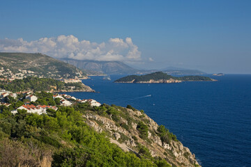 Panoramic view of Dubrovnik’s coastline, with its clear blue waters and lush green cliffs, under a sky with clouds.