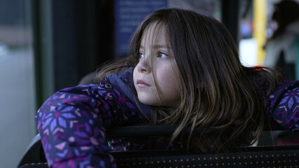 Contemplative little girl seated by bus window looking out with a thoughtful expression, closeup face of child daydreaming while traveling