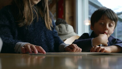 Closeup child hand picking food from restaurant menu, young siblings at diner deciding what to eat