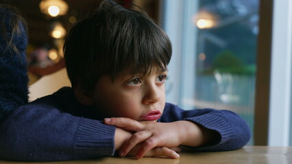 Pensive child feeling boredom at restaurant, leaning on table. Thoughtful little boy daydreaming, kid lost in thought - obrazy, fototapety, plakaty