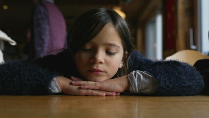 Sad thoughtful little girl feeling down while leaning on restaurant table, closeup of pensive...