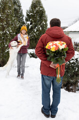 man hides a colorful large bouquet of flowers behind his back, and a happy woman stands in front of him in background, out of focus. Valentine's Day. Romantic relationship, surprise, feeling of love