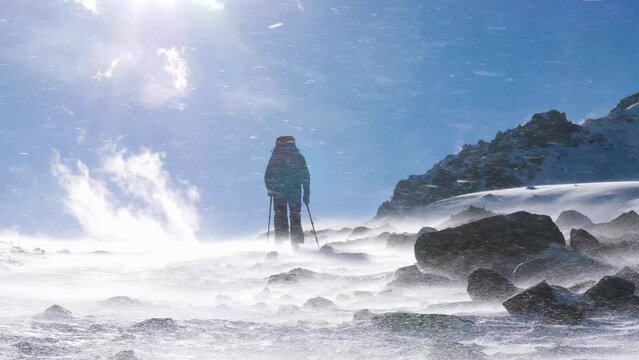 A man walks in the mountains on a windy day in winter. Snow crumbs are flying along the ground. Man with backpack and trekking poles. Slow Motion 2x