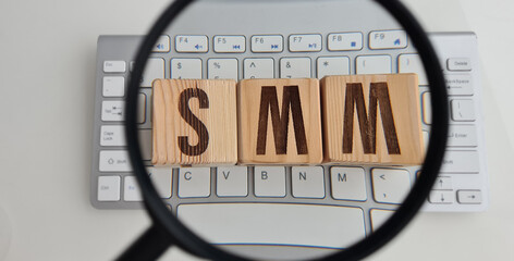 SMM abbreviation from wooden cubes on computer keyboard and magnifier