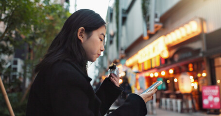 Phone, eating and Asian woman with onigiri in the city on exploring vacation, adventure or holiday. Hungry, food and young female person enjoying a Japanese snack or meal in town on weekend trip.