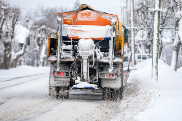 A snow-covered snowplow cleans the street after a snowfall, viw from back