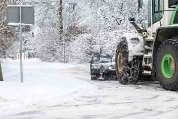 Tractor clears snow from road after snowfall, chains on tractor wheel, winter landscape