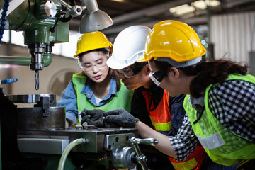 Asian foreman manager showing case study of factory machine to two engineer trainee young woman in...