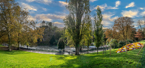 Paris, France - 11 11 2023: Park des Buttes Chaumont. View the central part of the park with footbridge, belvedere island, Temple of the Sibyl and the lake under construction due to renovation. - obrazy, fototapety, plakaty