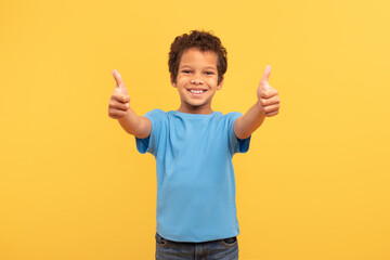 Joyful boy with double thumbs up in blue on yellow background