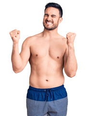 Fototapeta premium Young handsome man wearing swimwear very happy and excited doing winner gesture with arms raised, smiling and screaming for success. celebration concept.