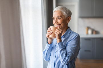 Mature gray lady with haircut sips tea holding cup indoor